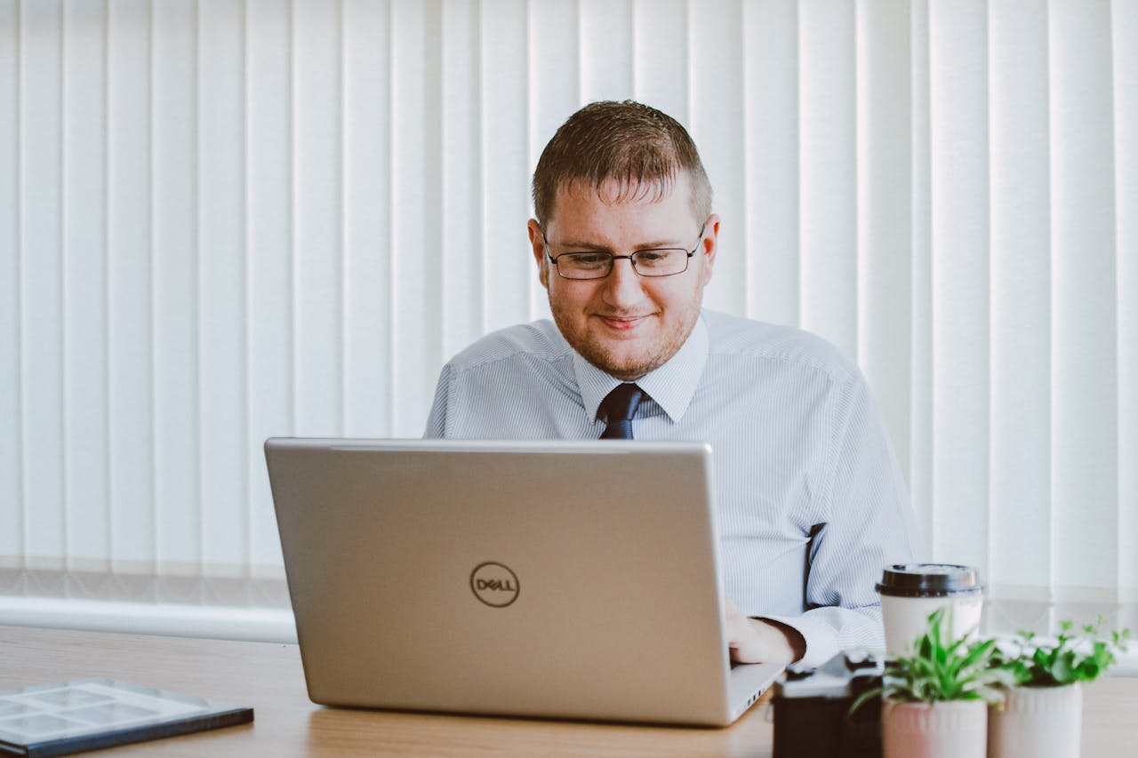 who-we-are-img Business professional working on laptop at office desk with coffee and plants.
